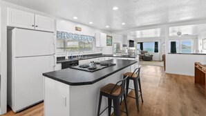 Una cocina moderna con una isla central, armarios blancos y vista al océano.