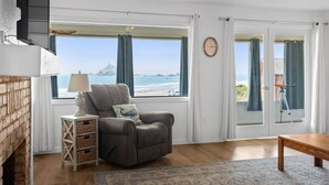 Una habitación con vistas al mar, chimenea, una silla, una lámpara y una mesa de madera.