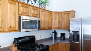 A modern kitchen with wooden cabinets, a stainless steel refrigerator, a microwave, a stove, and a coffee maker.