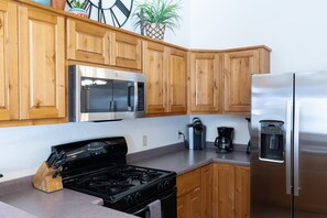 Cocina moderna con armarios de madera, un refrigerador de acero inoxidable, microondas, estufa y cafetera.