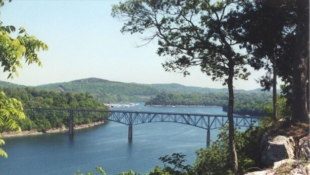 A bridge over a river with surrounding greenery and hills.