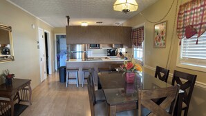 A modern kitchen with wooden cabinets, a central island, bar stools, and a dining table with chairs.