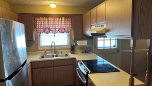 A compact kitchen with wooden cabinets, a stainless steel refrigerator, a double sink, and a black stove.