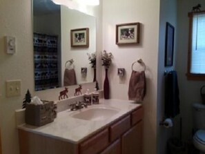 A bathroom with a large mirror, a sink, and a toilet. There are framed pictures on the wall and a towel rack.