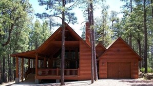 Eine Hütte mit Veranda, überdachter Terrasse und Garage, umgeben von hohen Kiefern.