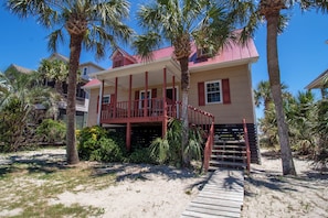A beachfront house with a red exterior, a wooden deck, and a staircase leading to a porch.