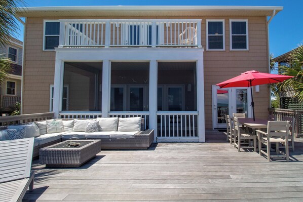 Une maison à deux étages avec un balcon, une terrasse couverte aménagée avec du mobilier et un parasol rouge.