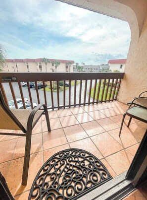 A balcony with a view of a parking lot and buildings, featuring a metal railing and two chairs. - Light and Bright 2 bedroom top floor condo with beach access, 2 pools (1 heated) (St. Augustine)