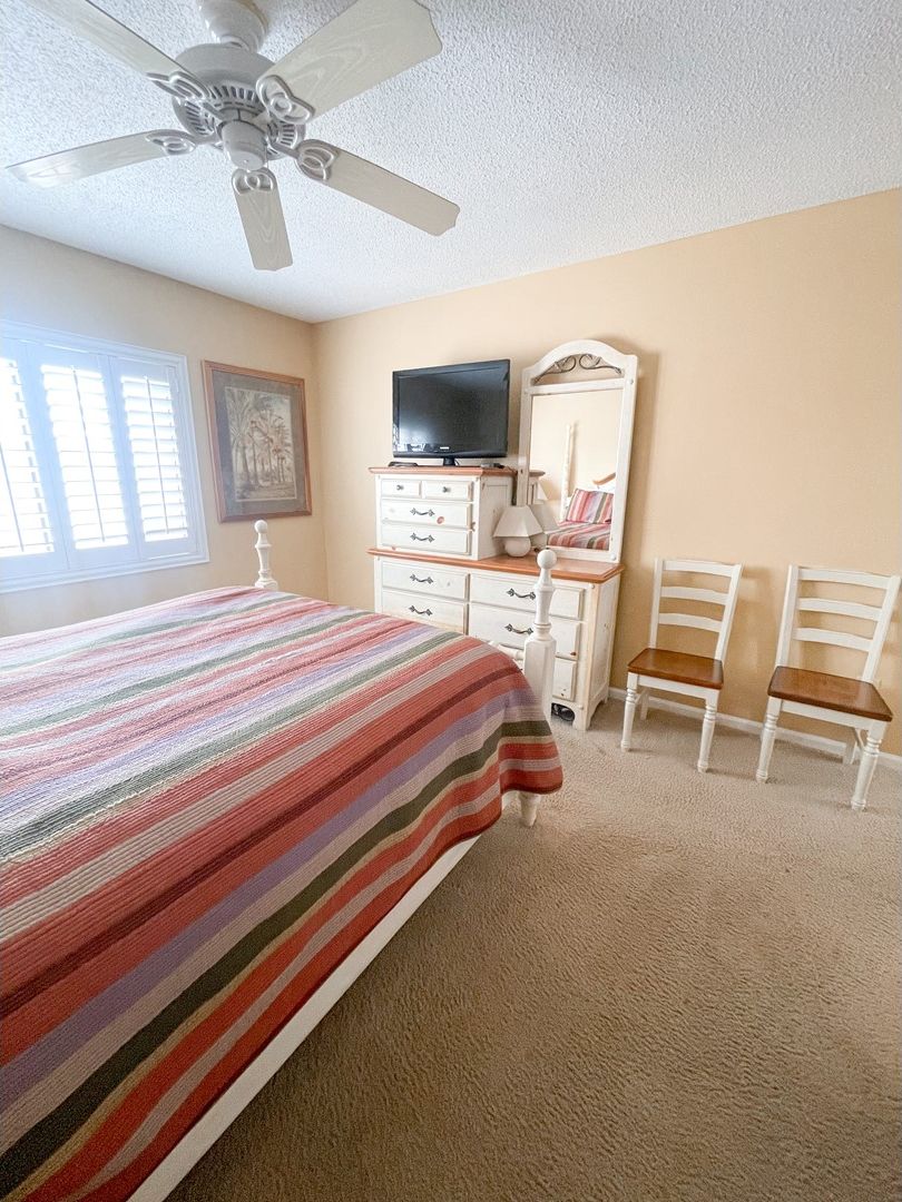 Une chambre à coucher comprenant un lit, une commode, des chaises, un téléviseur et un ventilateur de plafond.