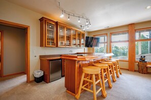 Una cocina con gabinetes de madera, un refrigerador empotrado, una barra con taburetes y ventanas amplias.