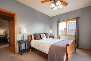 A bedroom with a bed, bedside tables, lamps, a ceiling fan, and a window with curtains.