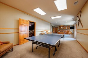 A room with a ping pong table, a wooden door, and a hallway leading to a kitchen area.