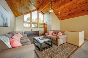 A spacious living room with a high ceiling, large windows, a ceiling fan, and a cozy seating area with a coffee table.