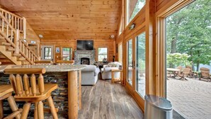 Ein Holzblockhaus-Interieur mit Kamin aus Stein, einem Essbereich aus Holz und großen Fenstern mit Blick ins Freie.