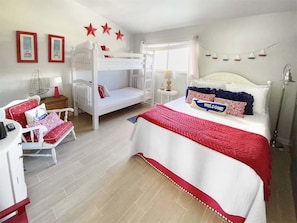 Quarto com uma cama beliche, um canape e uma escrivaninha, além de uma mesinha de cabeceira.