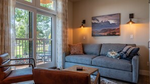 A cozy living room with a grey sofa, a leather chair, and a small table. There are two wall-mounted lamps and a painting above the sofa.