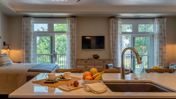 A hotel room with a bed, a dining table with fruit, a TV, and a view of the outdoors.