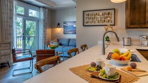 A modern kitchen with a central island, a dining area with chairs, a sofa, and a view of the outdoors.