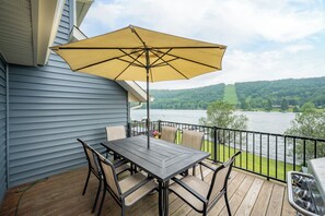 Een terras met een tafel, stoelen, een gele parasol en uitzicht op een meer en heuvels.
