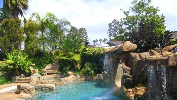 Una piscina con cascada, rodeada de vegetación tropical y rocas.