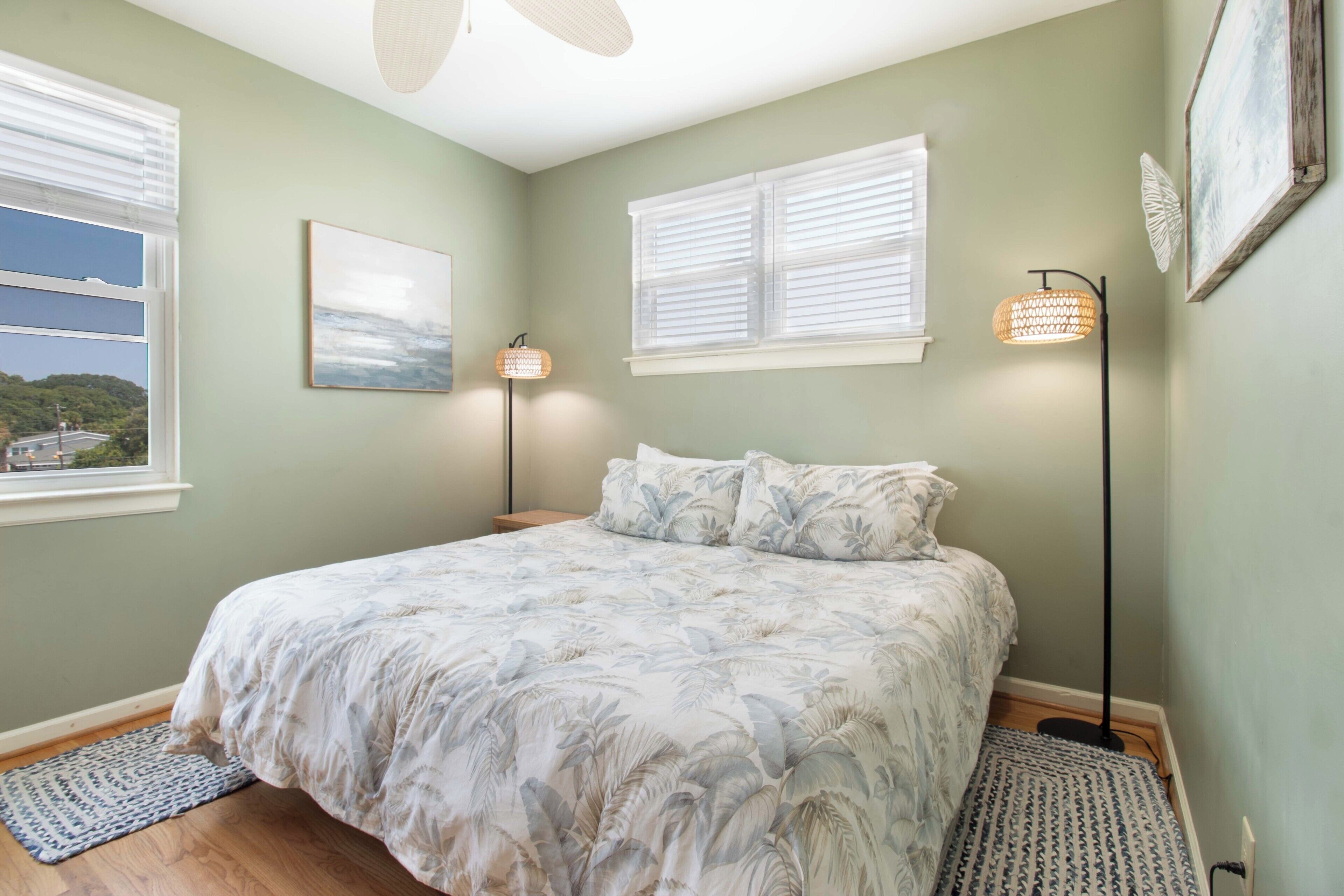 A bedroom with a bed, two bedside lamps, a window, and a wall-mounted picture.