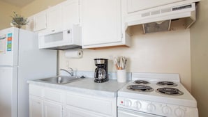 A kitchen with white cabinets, a stainless steel sink, a coffee maker, and a stove with four burners. - Oceanfront 1Br/1Ba Condo~Little Peace of Heaven (Folly Beach)
