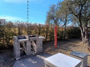 Un espacio al aire libre con una estructura de concreto, posiblemente una zona de estar, rodeado de árboles y un cielo despejado.
