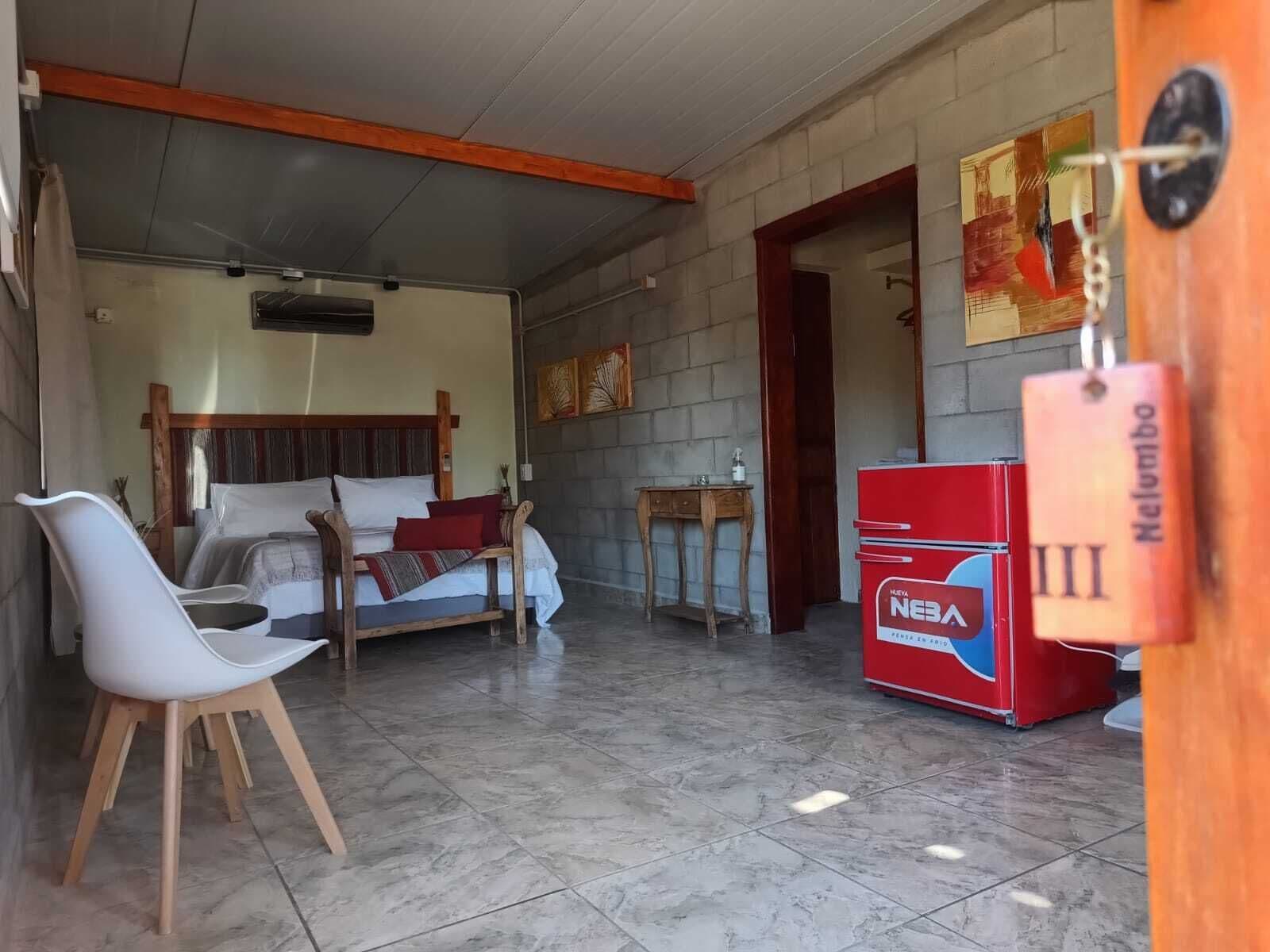 A hotel room with a bed, a desk, a chair, and a minibar.