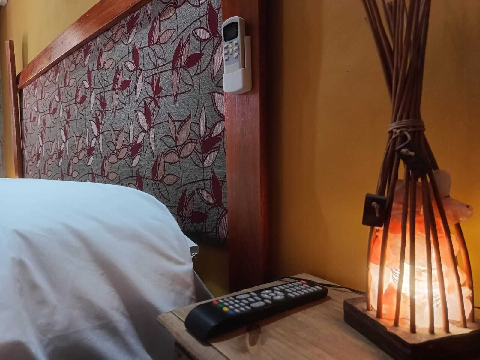A bed with a patterned headboard, a bedside table with a remote control, and a decorative lamp.