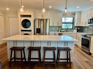 A modern kitchen with a large island, stainless steel appliances, and wooden bar stools.