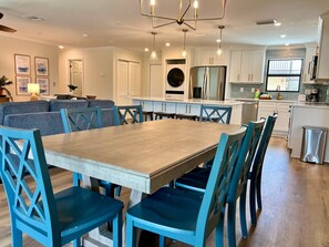 A modern kitchen with white cabinets, a stainless steel refrigerator, and a dining area with blue chairs and a wooden table.