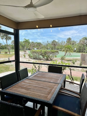 Un espace extérieur aménagé, abrité et doté d’une table et de chaises, offrant une vue sur un terrain de golf.