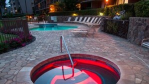 Un espace extérieur avec une piscine dont le sol est en pierre, agrémenté d’un jacuzzi au centre, entouré de chaises longues et d’un mur en pierre.