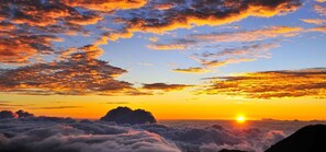 A sunset over a mountainous landscape with clouds below.