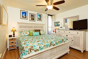 A bedroom with a bed, a nightstand, a dresser, a ceiling fan, and framed pictures on the wall.