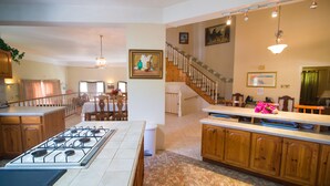 A kitchen with a gas stove, wooden cabinets, a dining area with a table and chairs, and a staircase leading to another level.