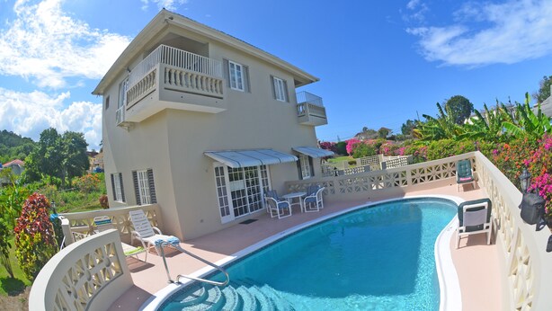 A two-story building with a swimming pool, outdoor seating, and a view of the surrounding landscape.