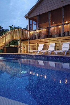 Un área de piscina con sillas de descanso y una terraza de madera con barandilla.