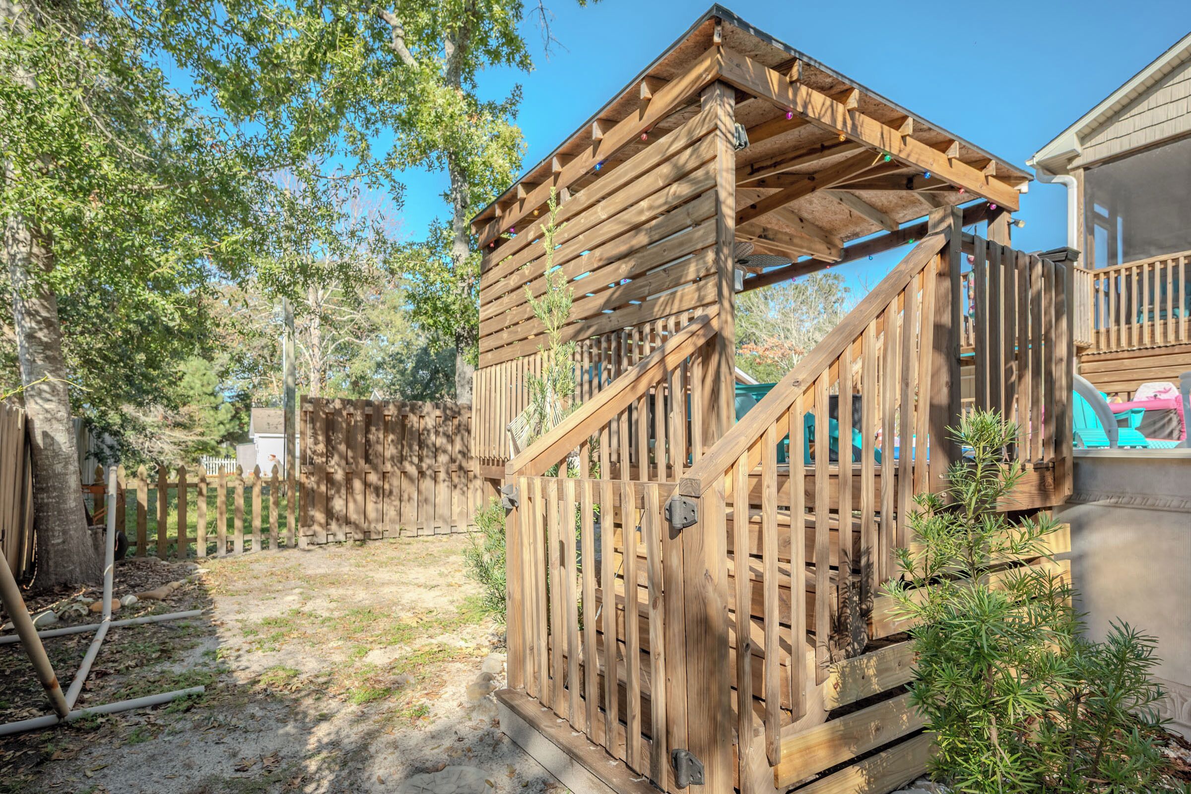 Una terraza de madera con una pérgola, un patio cercado y un árbol pequeño.