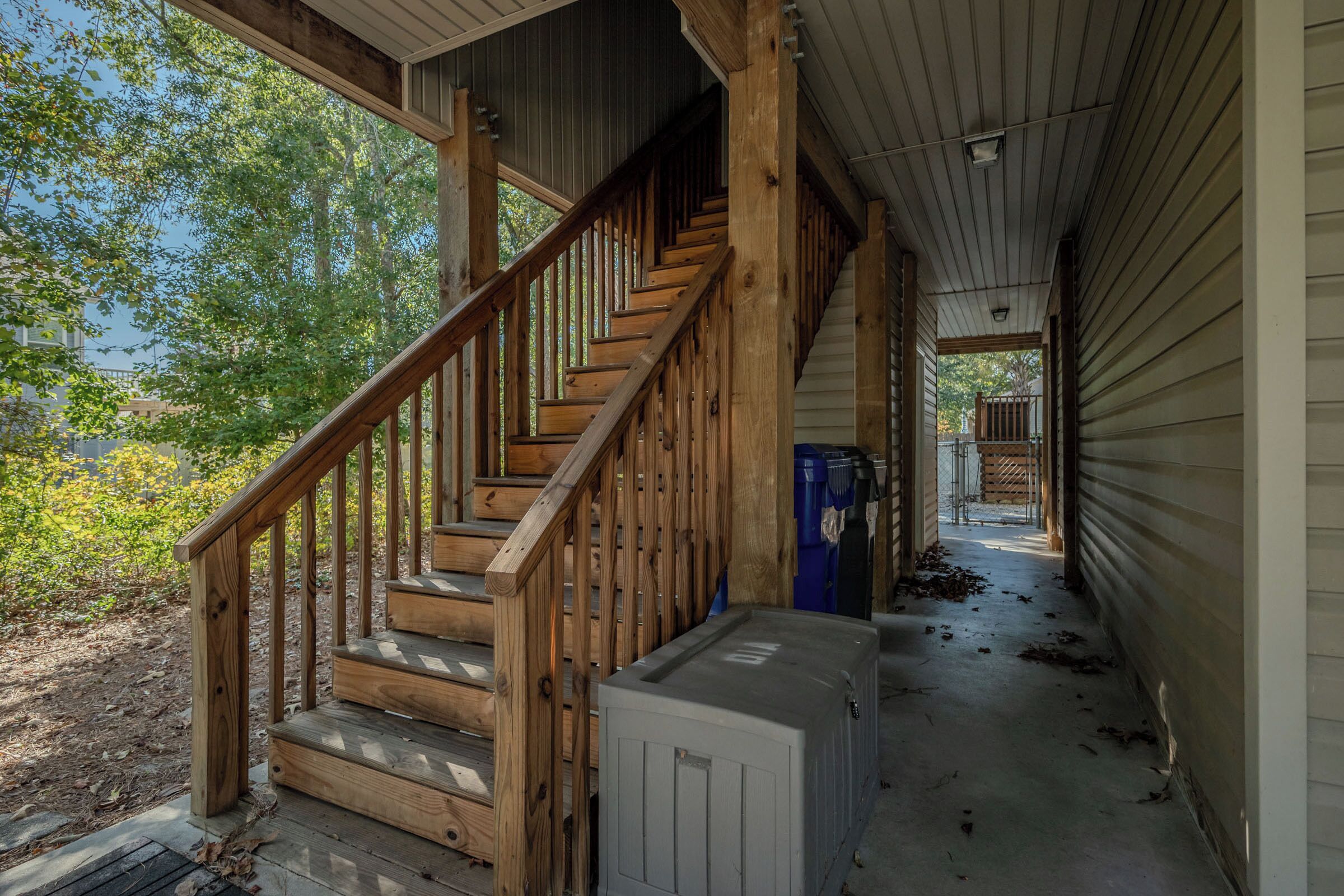 Un escalier en bois mène à un porche abrité d’où l’on peut admirer les arbres et un bâtiment situé au loin.