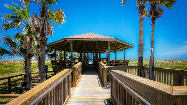 A wooden boardwalk leading to a covered pavilion with benches and a view of the ocean.