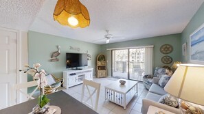 Relax in this stylish living room with a flat-screen TV, ceiling fan, and large window offering a view of the outside.