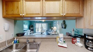 A kitchen with wooden cabinets, a granite countertop, stainless steel sinks, and various kitchen appliances.