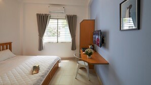 Une chambre à coucher avec un lit, un bureau avec une chaise, une fenêtre avec des rideaux et un tableau encadré au mur.