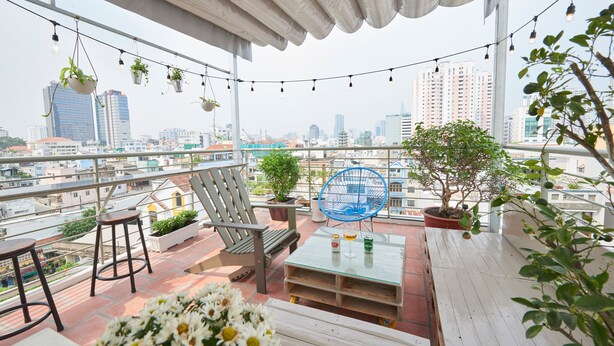 Un balcon offrant une vue sur la ville, avec une table, des chaises, des plantes suspendues et un arbre en pot.