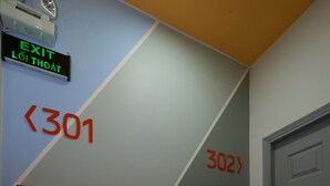 Un couloir avec des panneaux indiquant les sorties, des portes numérotées et du matériel de sécurité incendie.