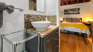 A bathroom with a glass shower enclosure, a white sink, and a mirror with lights. - Tiny House in Alameda/Alberta Arts ~ Dog Friendly (Portland)