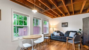 A room with a wooden ceiling, a round table with chairs, a sofa, and a window with a view of greenery. - Tiny House in Alameda/Alberta Arts ~ Dog Friendly (Portland)