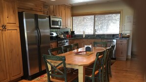 Una cocina con armarios de madera, un refrigerador de acero inoxidable, un microondas y una mesa de comedor con sillas.