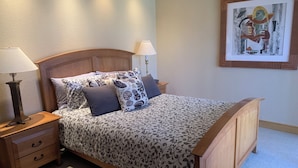 Una cama bien tendida con ropa de cama estampada, cabecera de madera y mesitas de noche con lámparas.